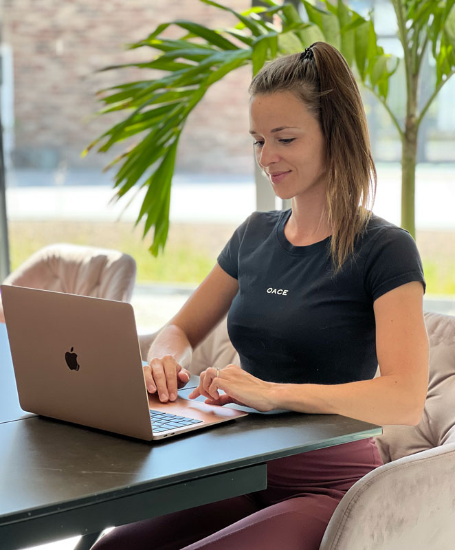 Ein Foto der Coach, die in einem sonnigen Raum sitzt und an ihrem Laptop am Online Coaching arbeitet.